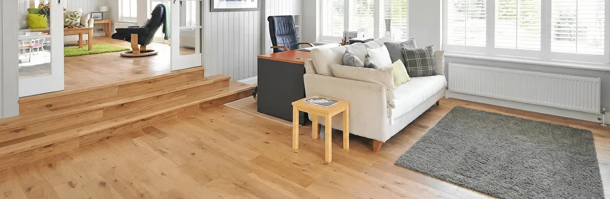 A modern living room with professionally installed laminate flooring, a beige sofa, a small side table, a gray rug, and large windows with white shutters in Fort Worth, TX